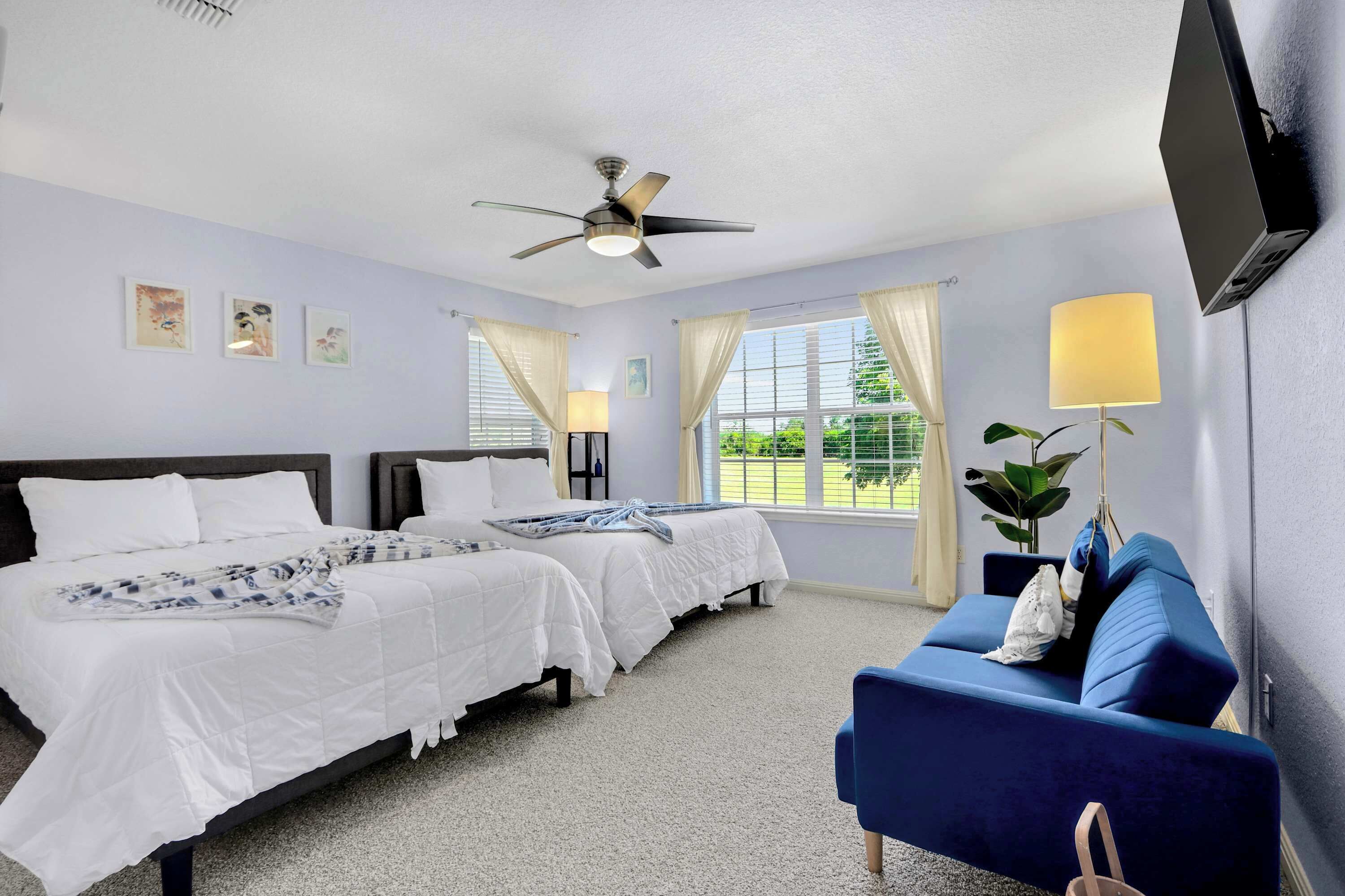 A hotel room with two beds, a blue sofa, a ceiling fan, and a TV mounted on the wall.