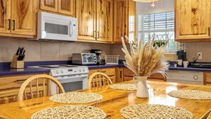 A kitchen with wooden cabinets, a microwave, a stove, and a dining table with placemats. - Spacious Retreat & Game Room Sleeps 12 (New Braunfels)