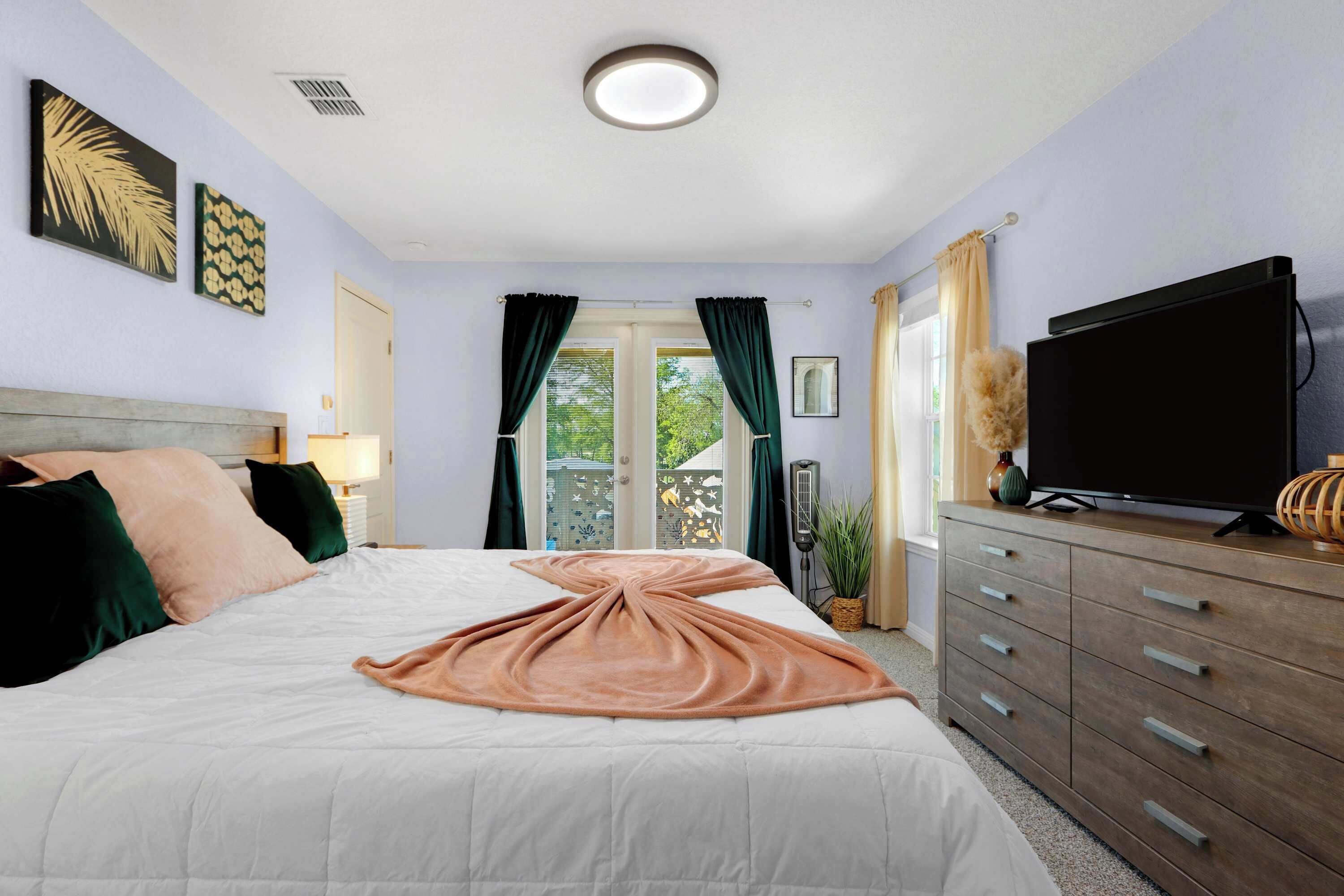 A bedroom with a bed, a dresser, a television, and a window with curtains.