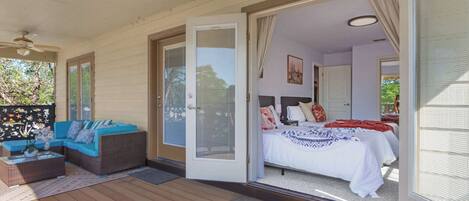 A room with a bed, a sofa, and a sliding glass door leading to an outdoor area with a wooden deck.