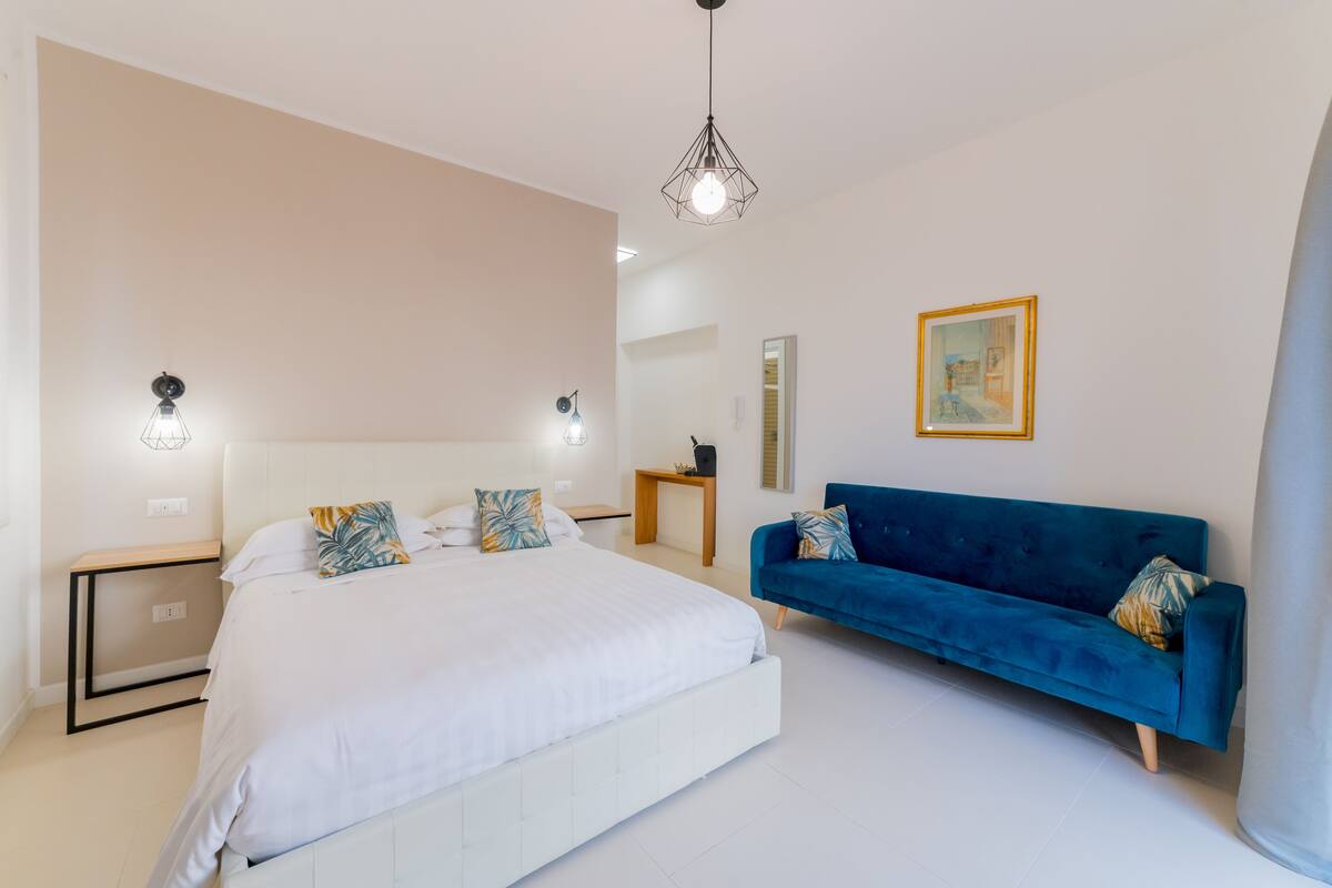 A modern bedroom with a large bed, a blue sofa, and a pendant light.