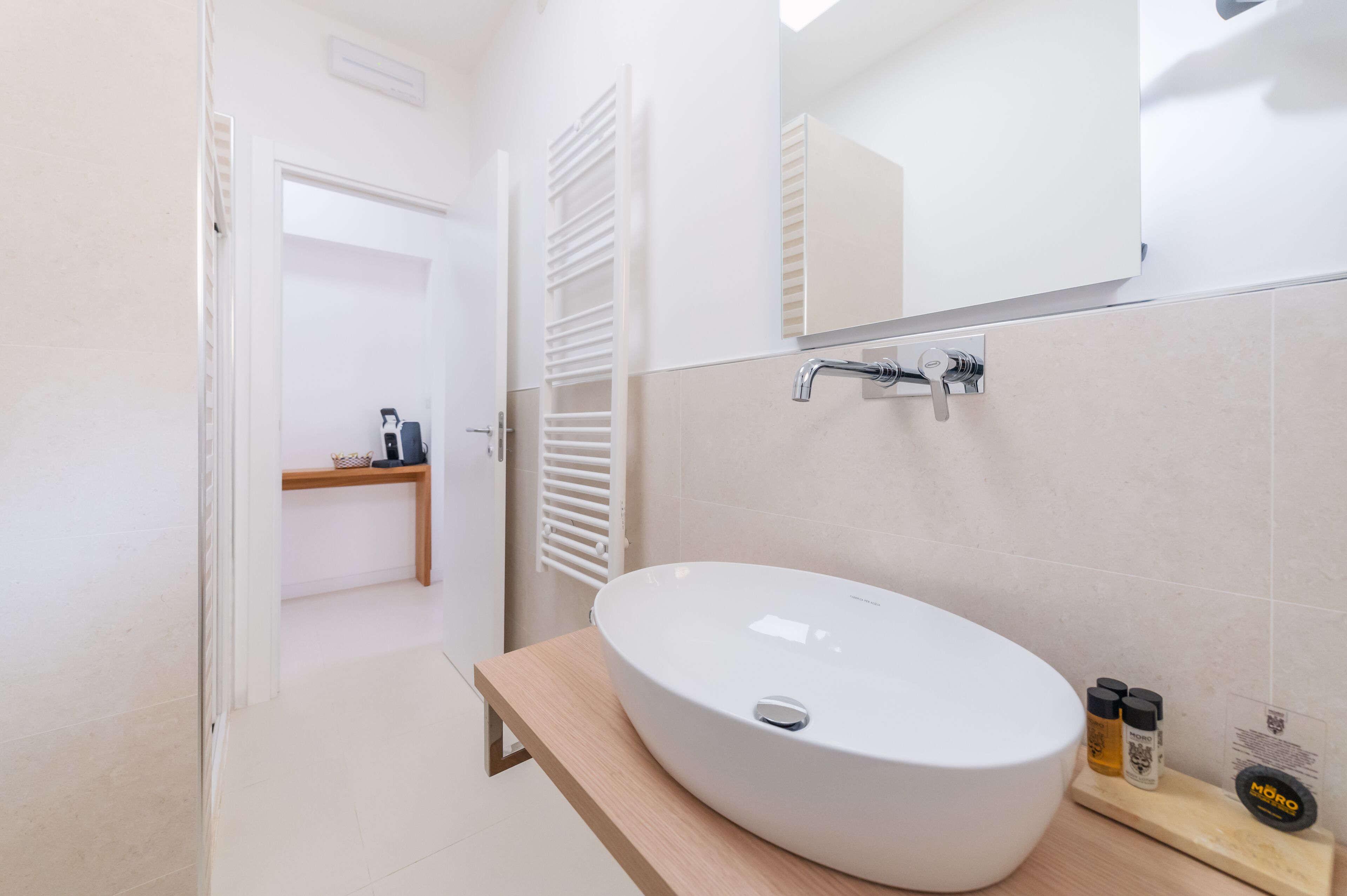 A modern bathroom with a large oval sink, a mirror, and a towel rack.