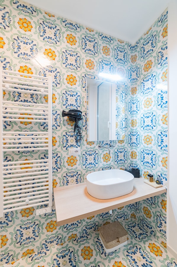 A bathroom with a white sink, a mirror, a towel rack, and patterned wallpaper.