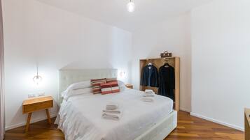 A neatly made bed with white linens, a wooden nightstand, a wooden wardrobe, and a hanging light fixture.