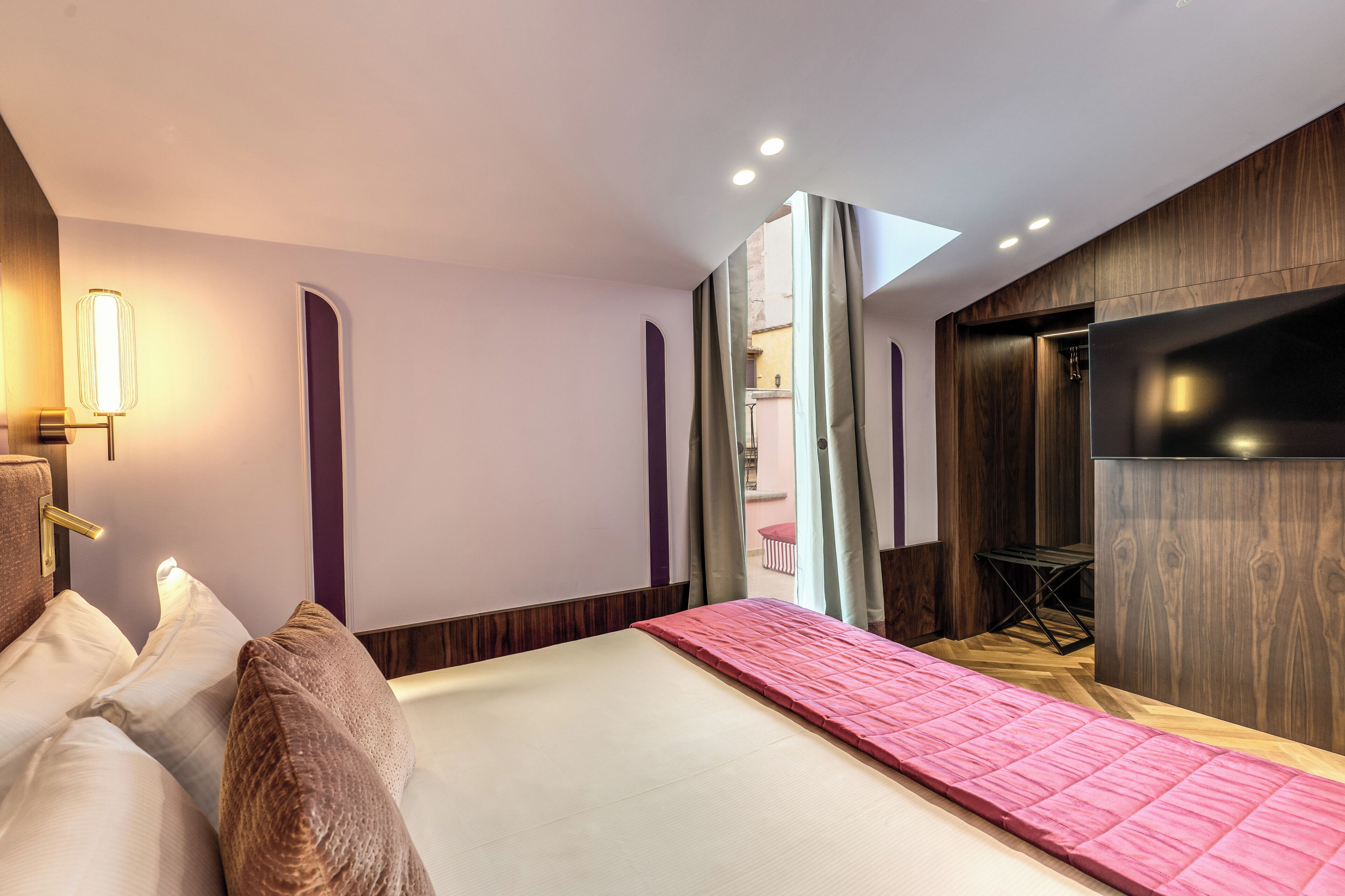 A modern hotel room with a bed, a desk, and a view of the outside.