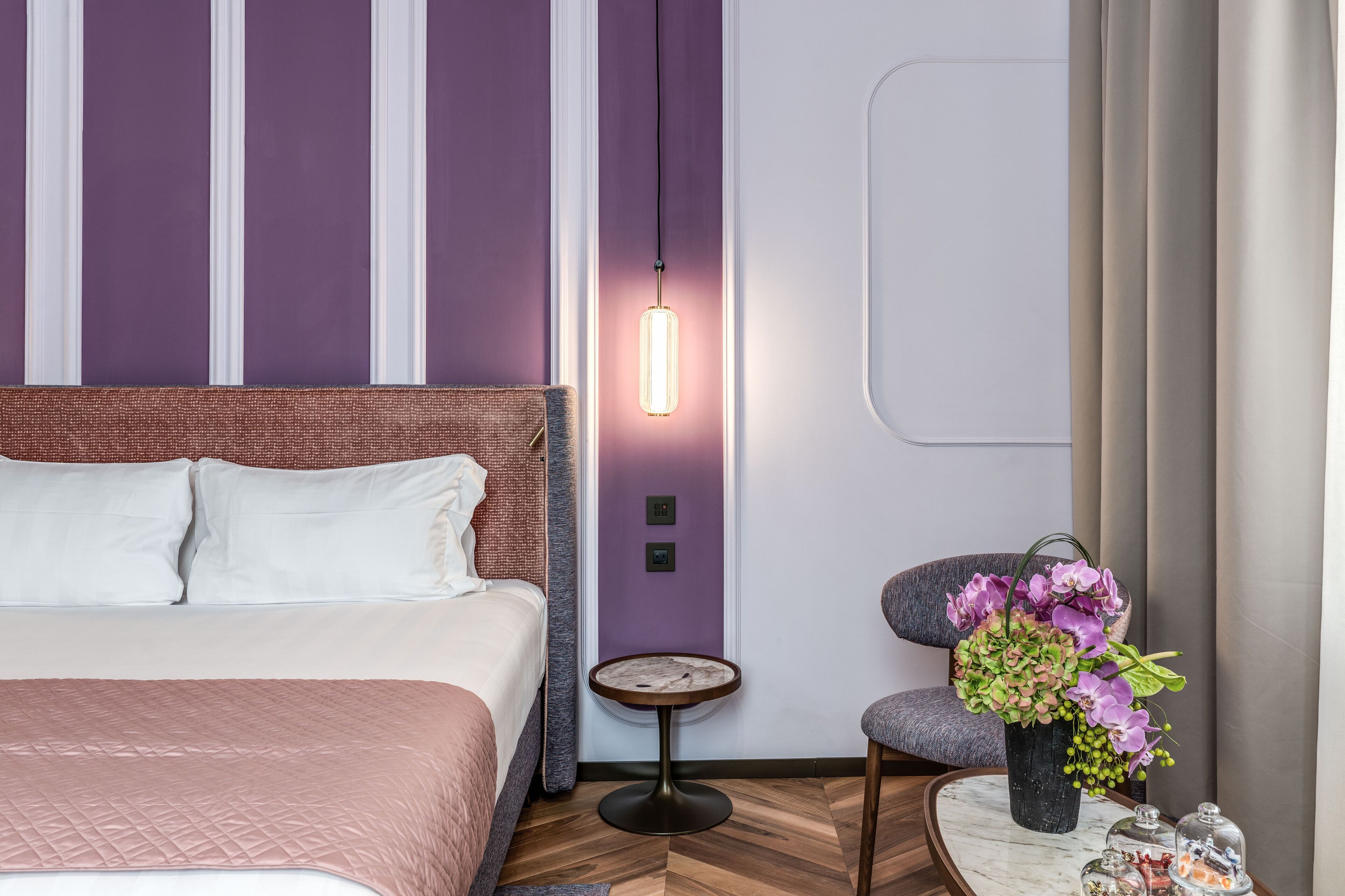 A modern hotel room with a large bed, a small round table with a vase of flowers, and a chair.