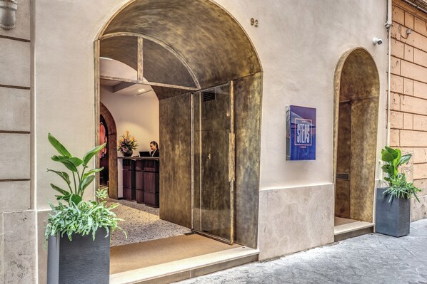 A hotel entrance with a modern design, featuring a glass door, a reception area visible through an archway, and potted plants at the entrance. - THE STEPS Hotel - by Eitch Collection (Rome)