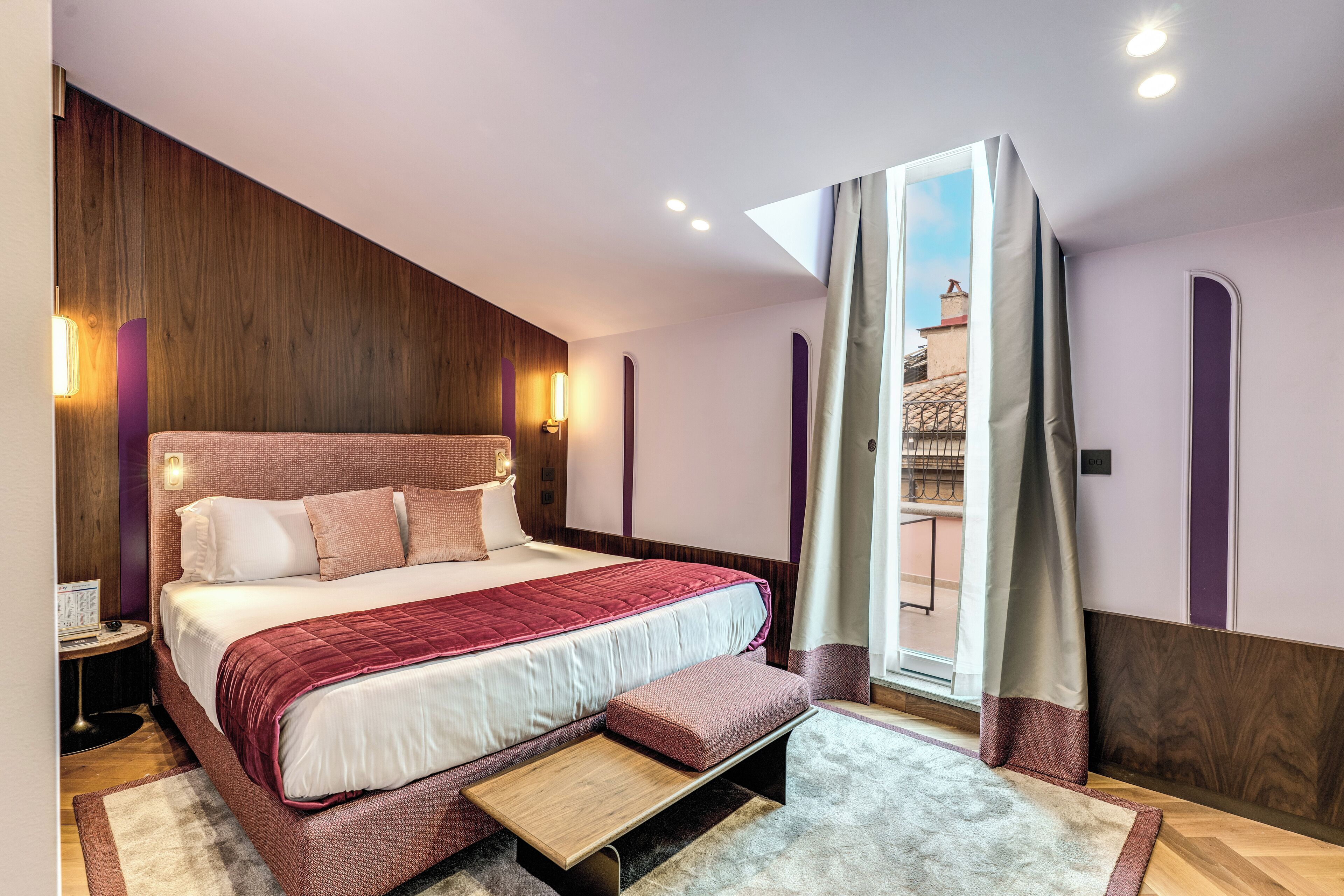 Un dormitorio moderno con una cama grande, un banco y vistas a la ciudad.
