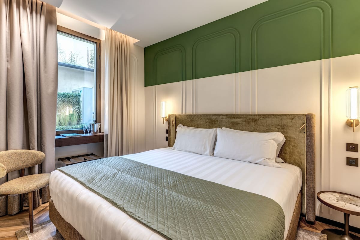 Una cama bien hecha con colcha verde, cabecera de madera y mesita de noche con lámpara.