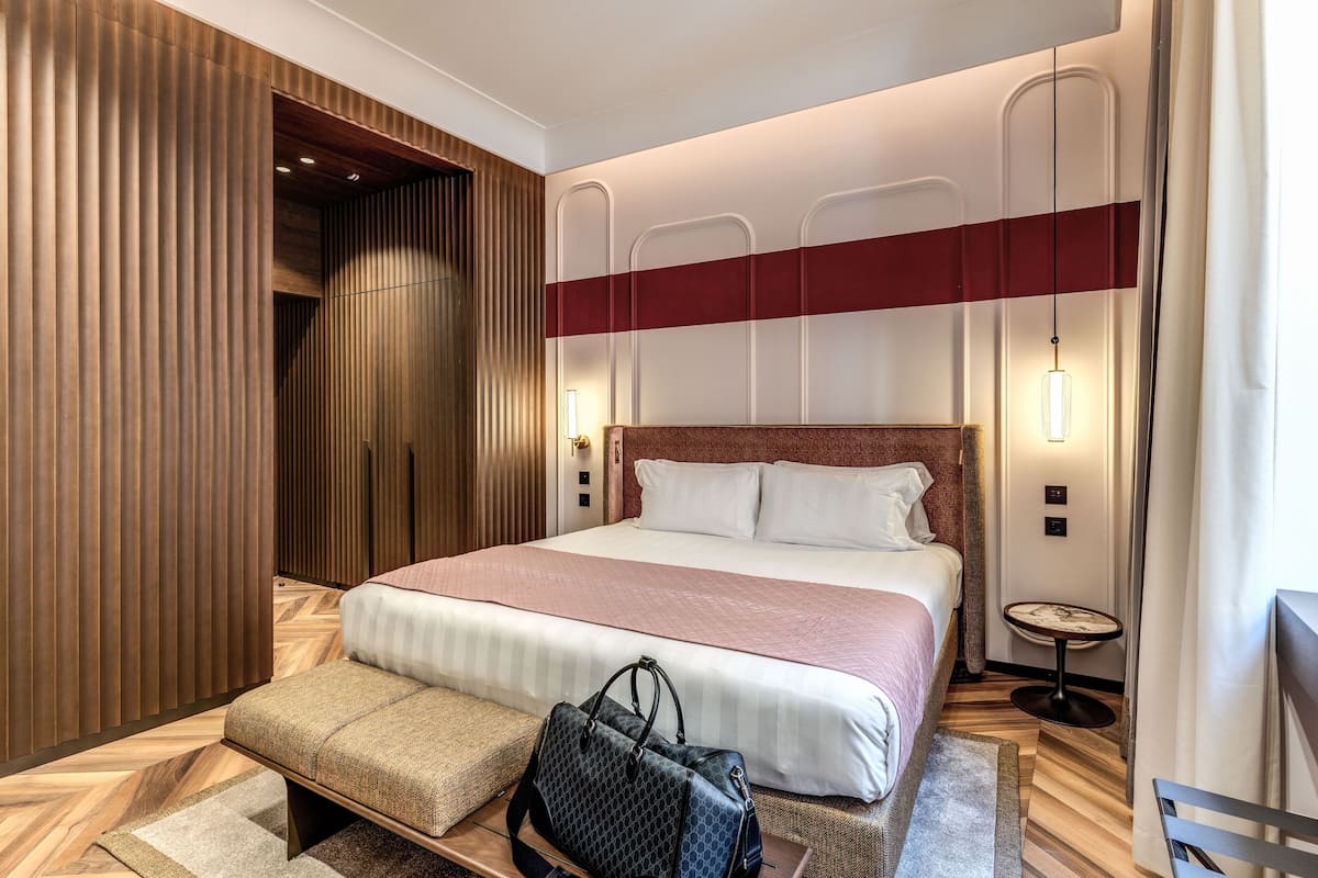 Habitación de hotel con una cama grande, paneles de madera, una mesita redonda y un banco.