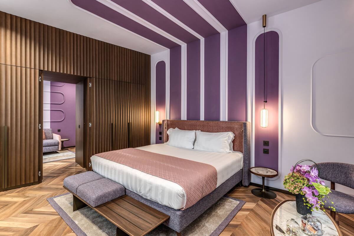 Un dormitorio moderno con una cama grande, un banco, una mesita pequeña y una silla.