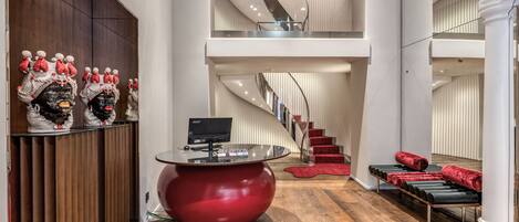 A modern reception area with a red reception desk, a staircase, and a seating area with red cushions.