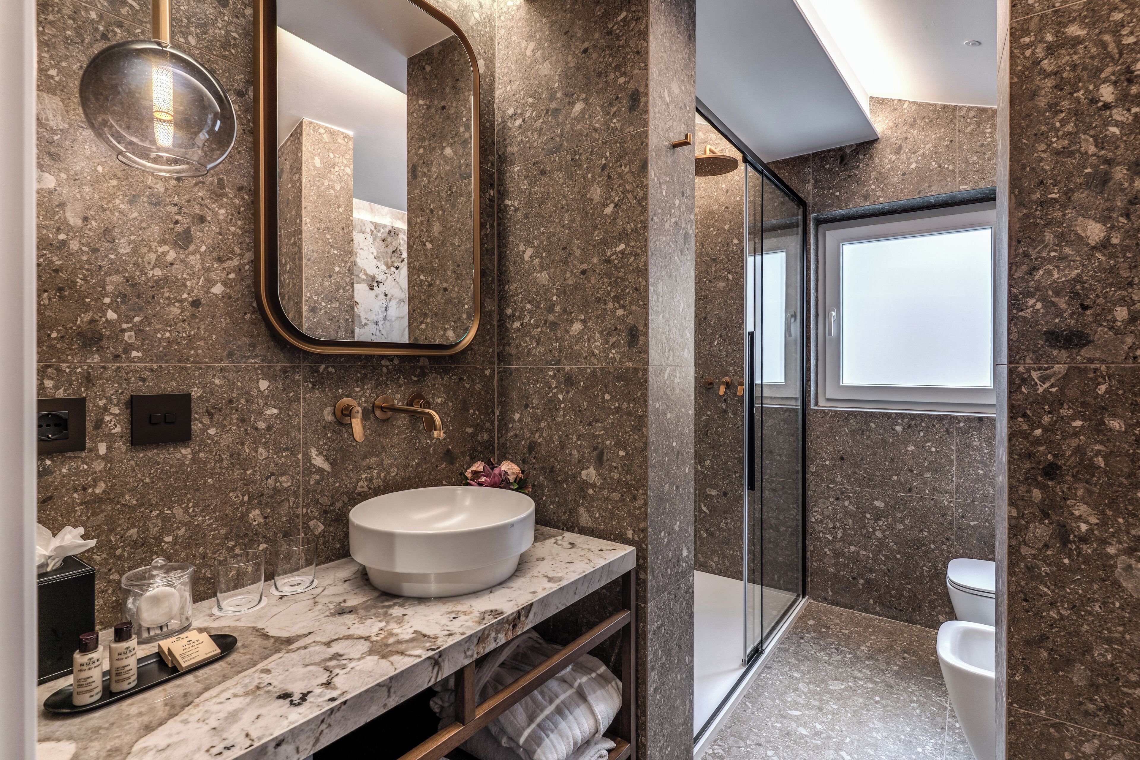 A modern bathroom with a marble sink, a large mirror, and a glass shower enclosure.