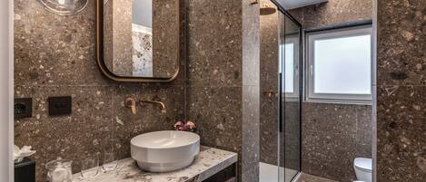 A modern bathroom with a marble sink, a large mirror, and a glass shower enclosure.
