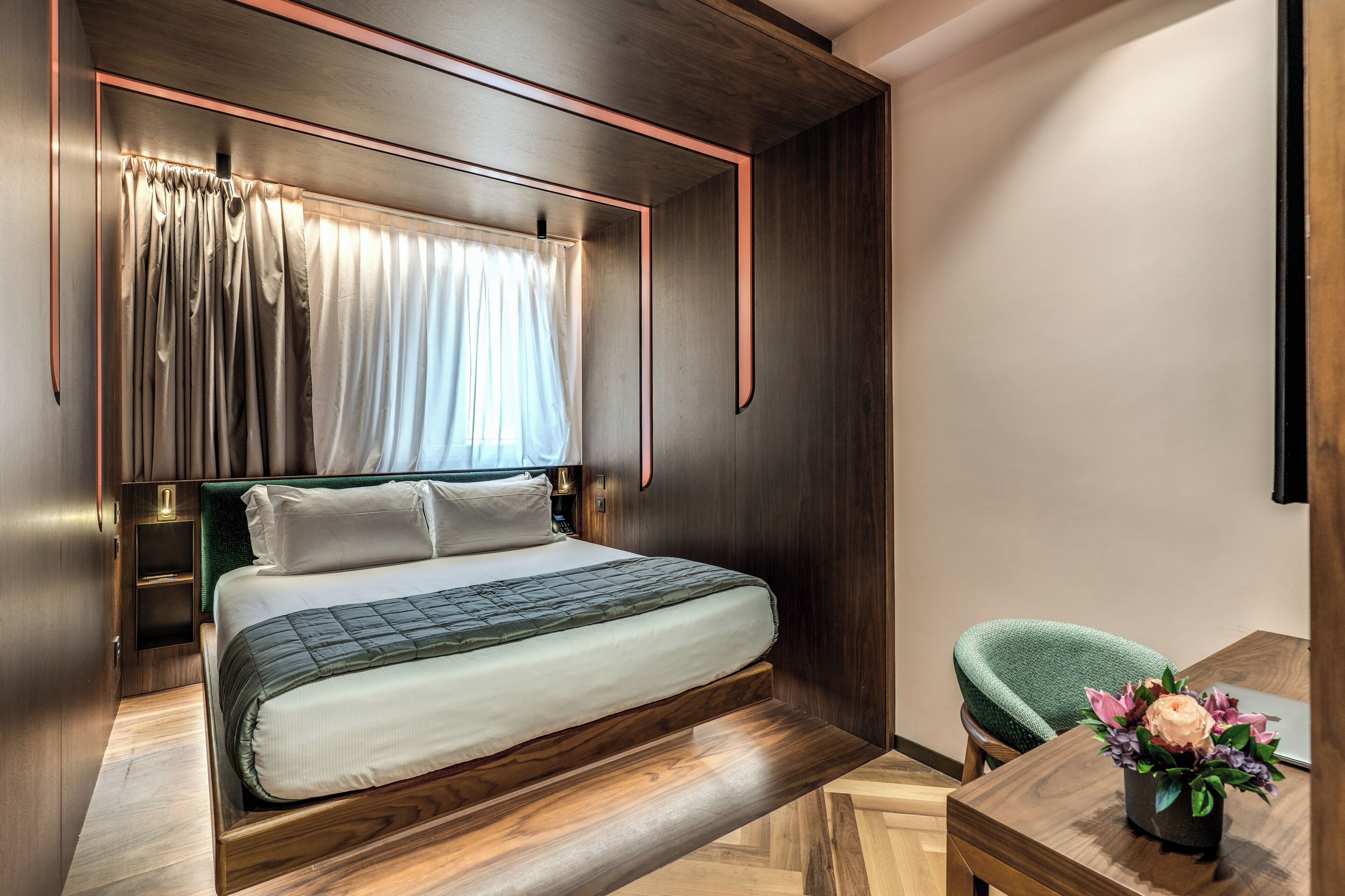 A modern bedroom with a wooden bed, a green chair, and a small table with a flower vase.