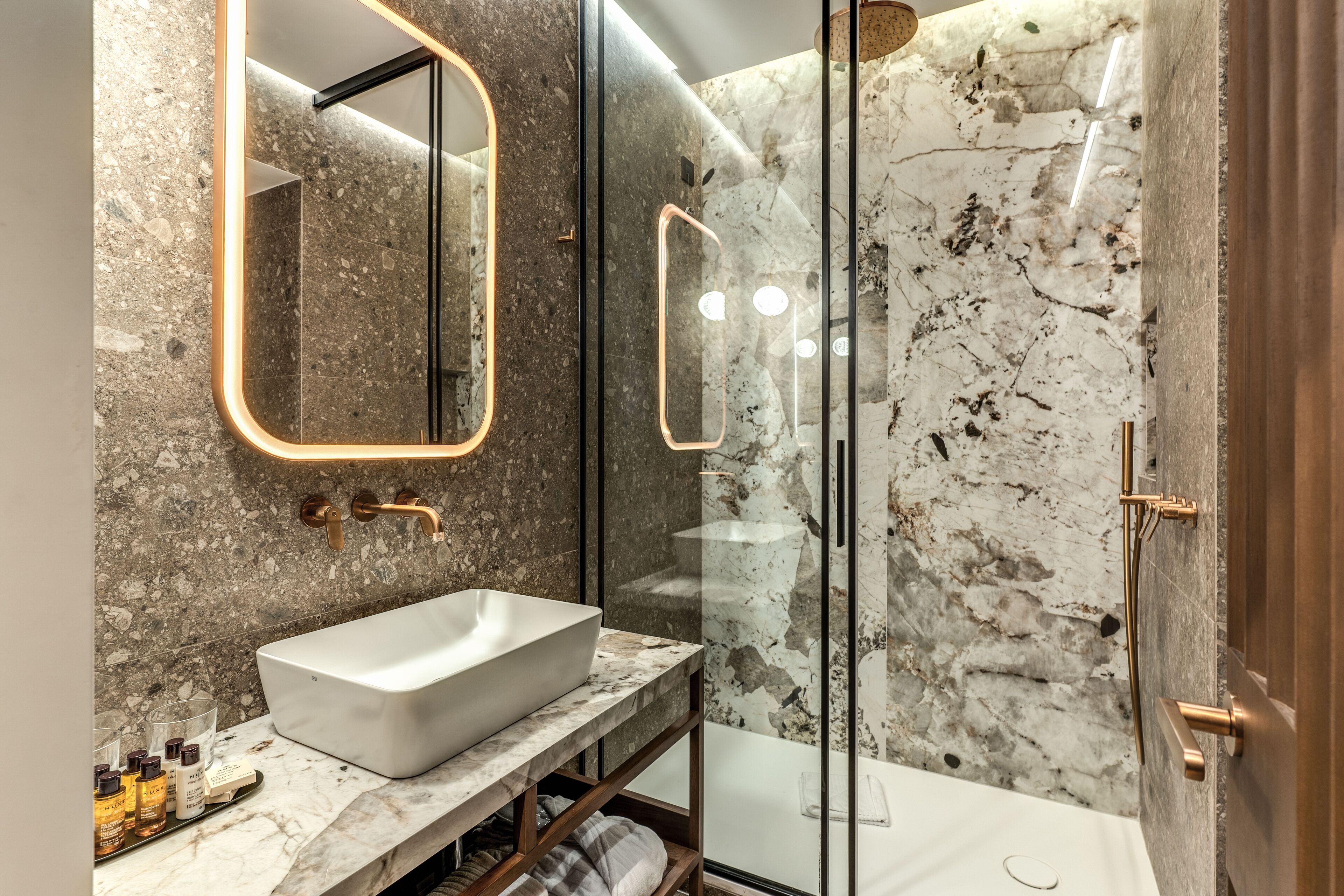Un baño moderno con un lavamanos grande de color blanco, paredes de mármol y ducha con cerramiento de vidrio.