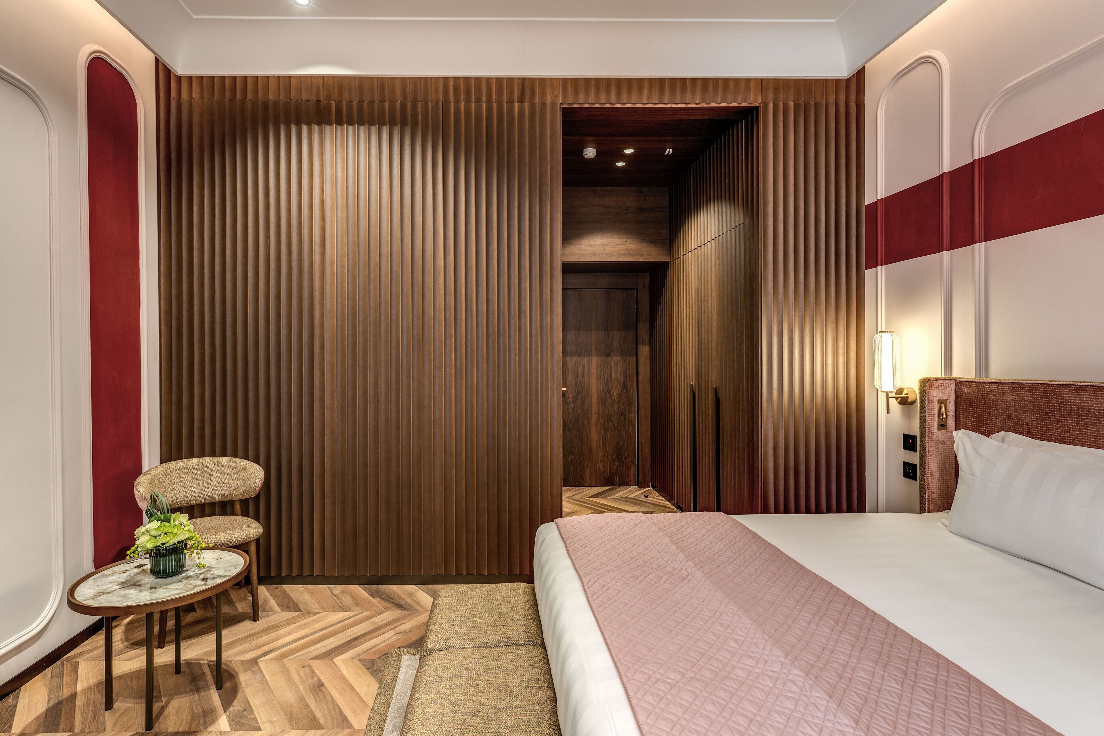 A hotel room with a bed, a small round table with a plant, a chair, and a wooden partition wall.