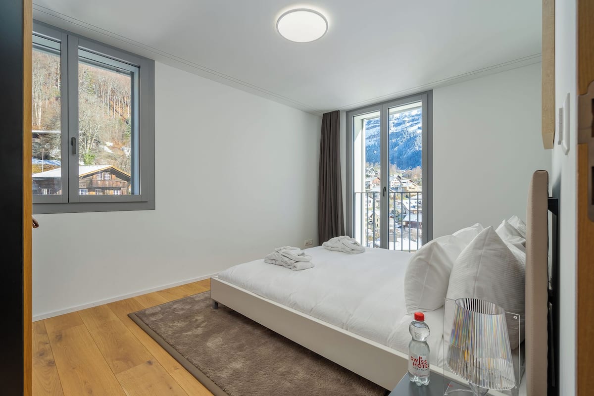 A bedroom with a bed, a window with a view of a mountain, and a bottle of water on a table.