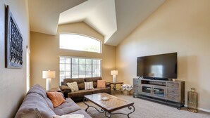 Ein geräumiges Wohnzimmer mit hoher Decke, einem großen Fernseher und einer gemütlichen Sitzecke mit Sofas und einem Couchtisch.