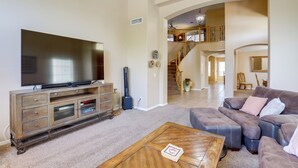 Ein geräumiges Wohnzimmer mit einem großen Flachbildfernseher, einer Holztrenneinrichtung, einem grauen Ecksofa und einer Treppe, die in ein Obergeschoss führt.