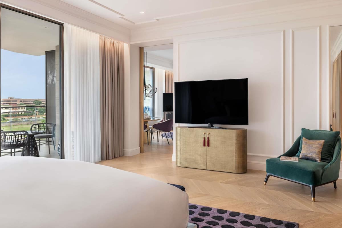 Een hotelkamer met een groot bed, een televisie op een kast, een groene fauteuil en uitzicht op het omliggende landschap.