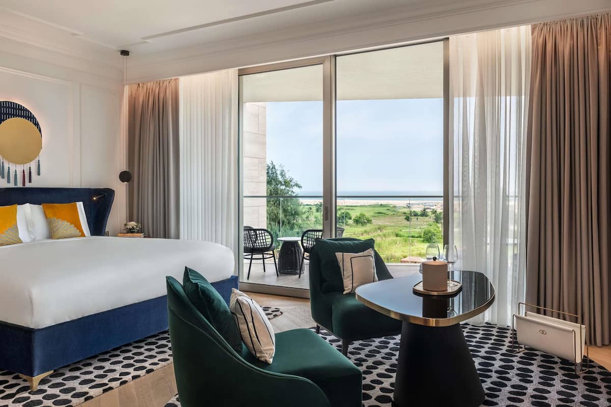 Een hotelkamer met een bed, een slaapbank, een tafel en uitzicht op het strand.