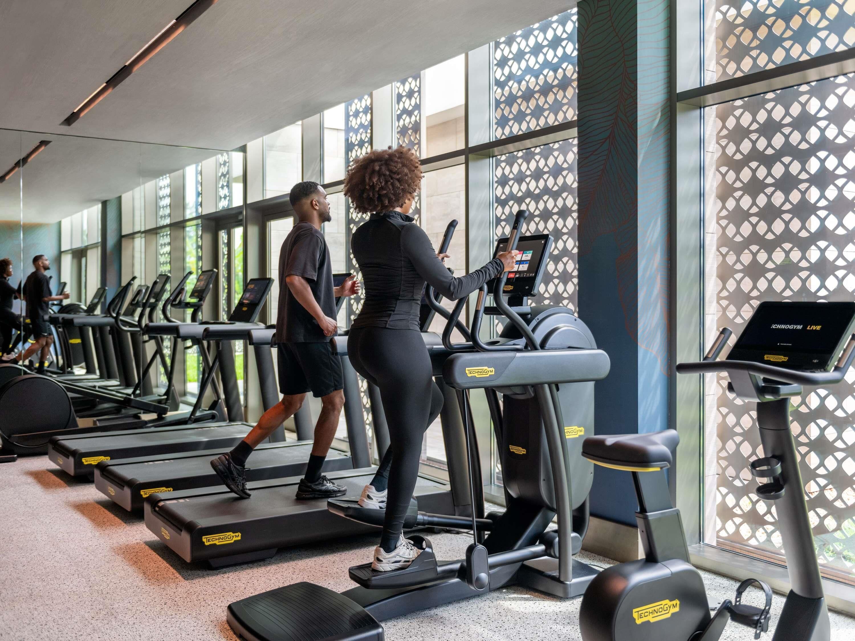 A gym with treadmills, a digital screen, and large windows.