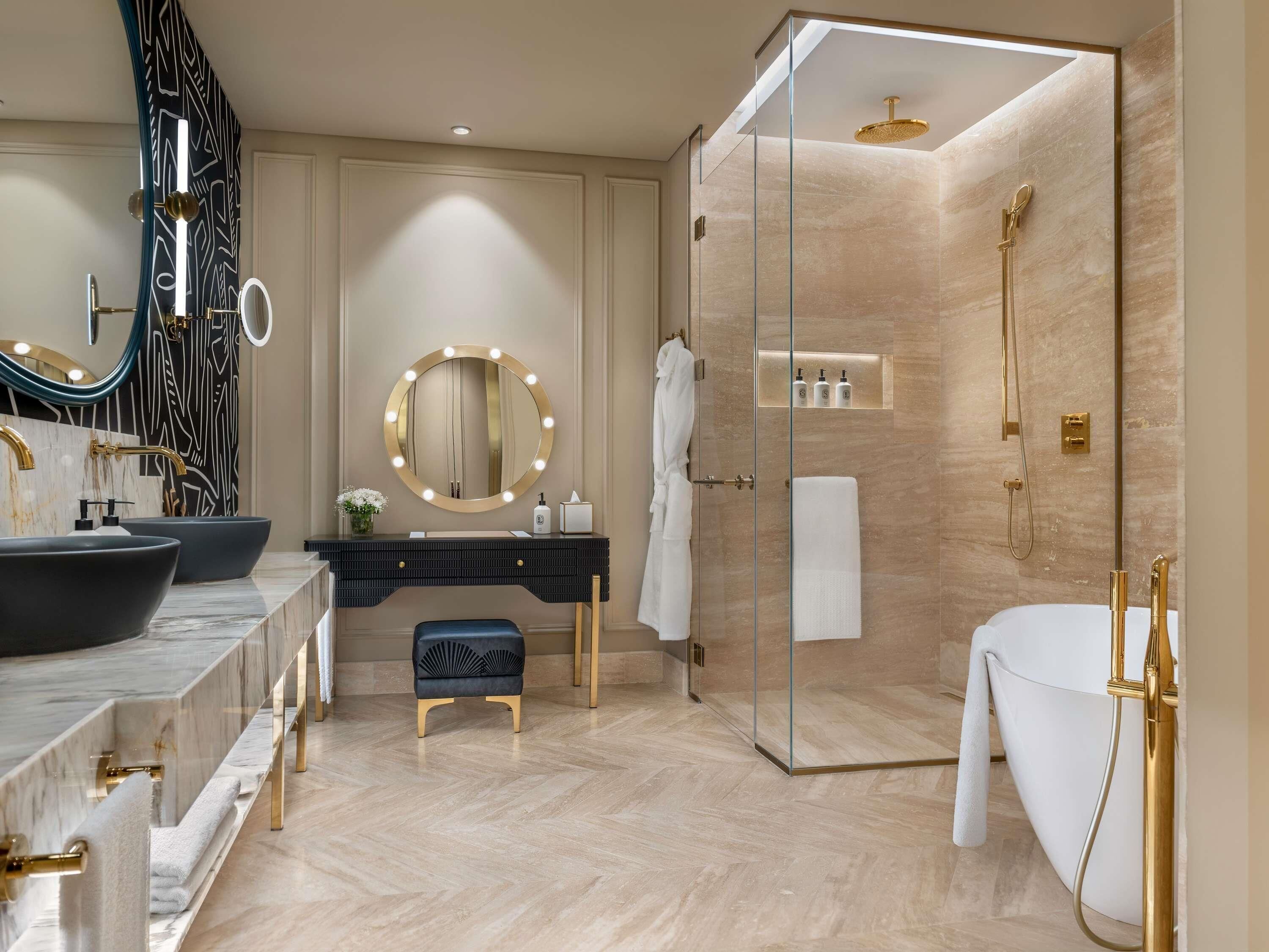 A modern bathroom with a vanity, two sinks, a large mirror, a walk-in shower, and a bathtub.