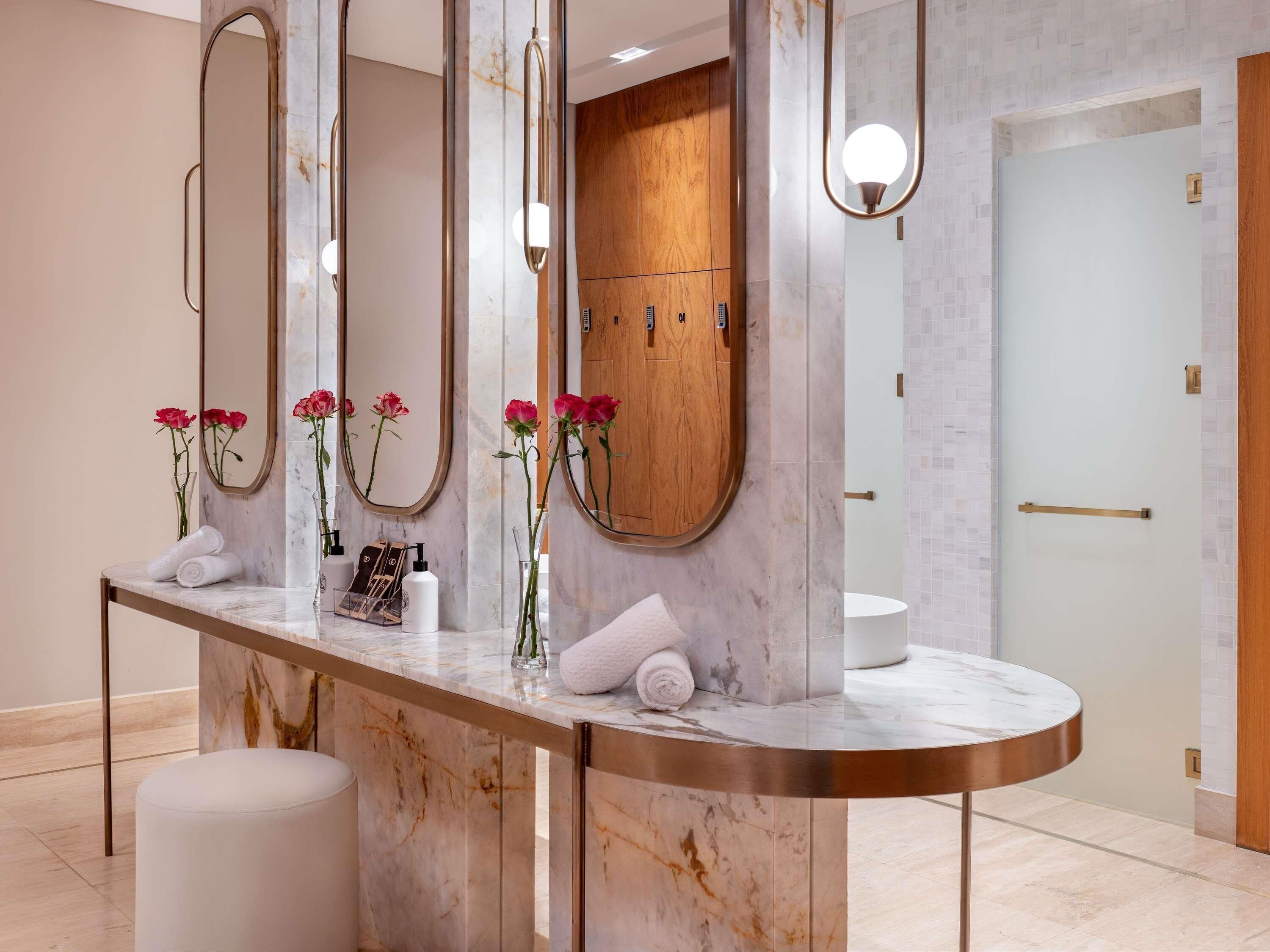 Une salle de bain moderne avec des comptoirs en marbre, plusieurs miroirs, un meuble en bois et un lavabo rond.