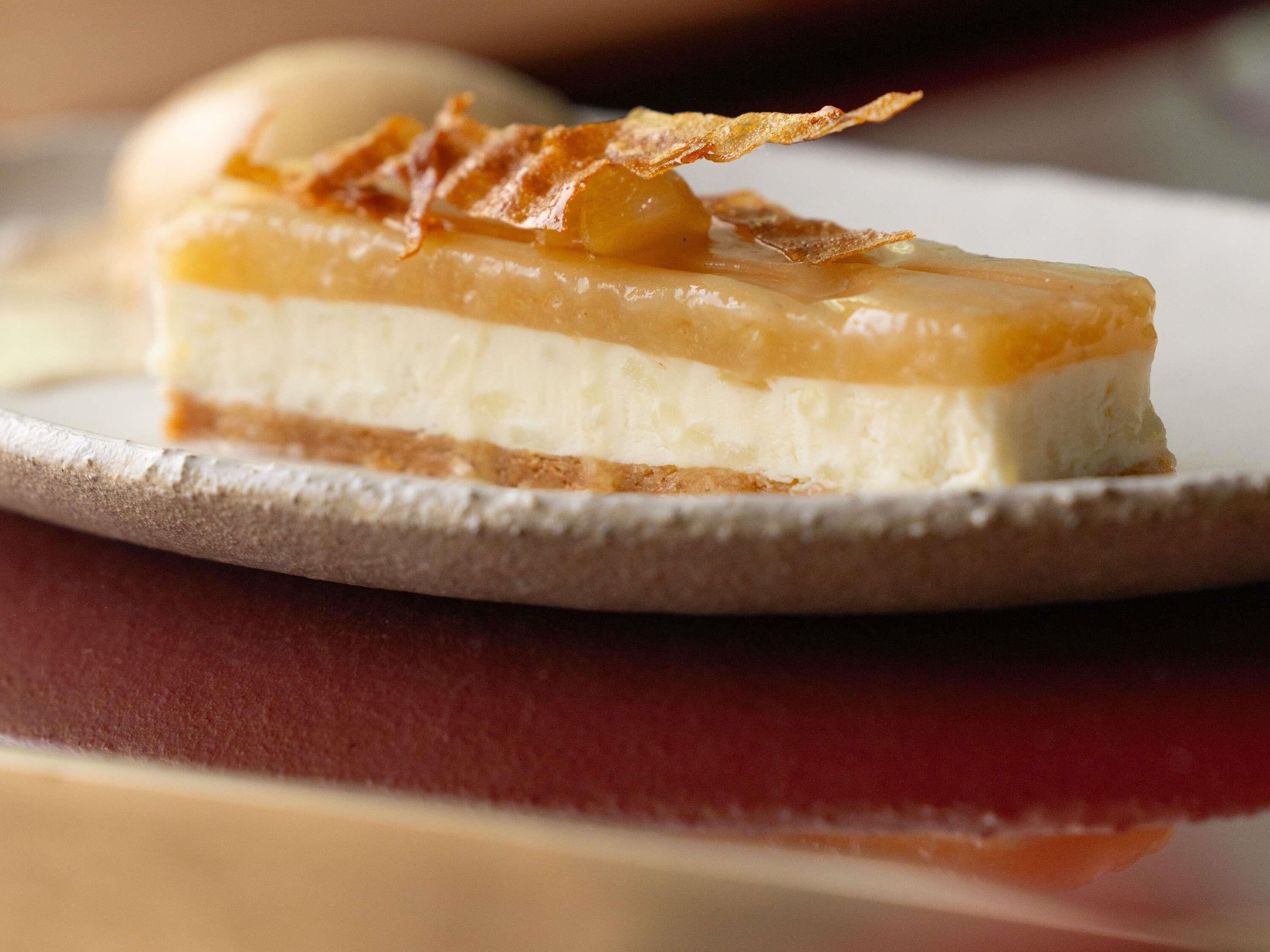Una porción de pastel de queso con cobertura de caramelo y una galleta crujiente sobre un plato.