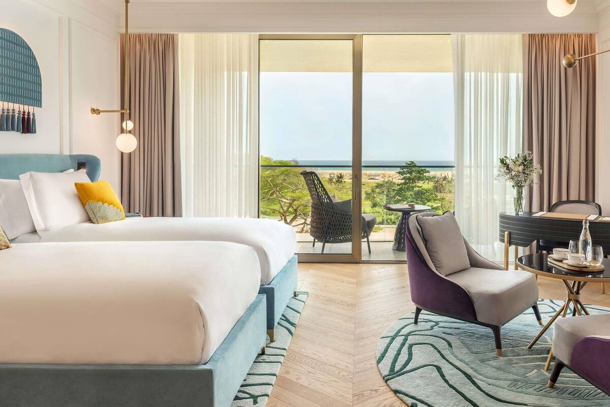 Een moderne hotelkamer met een groot bed, een zithoek met een tafel en een balkon met uitzicht op het strand.