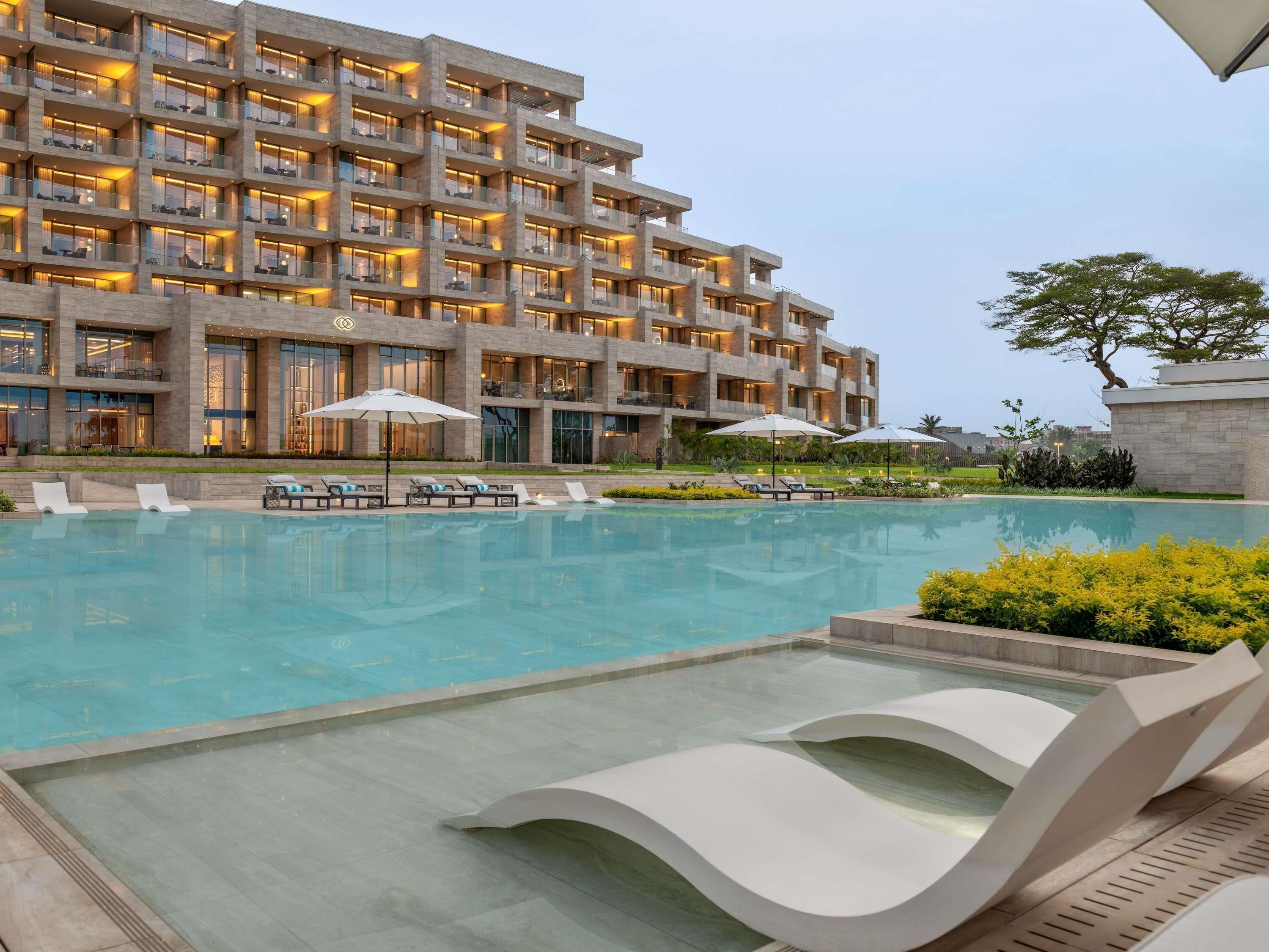A modern hotel with a large pool, sun loungers, and umbrellas.
