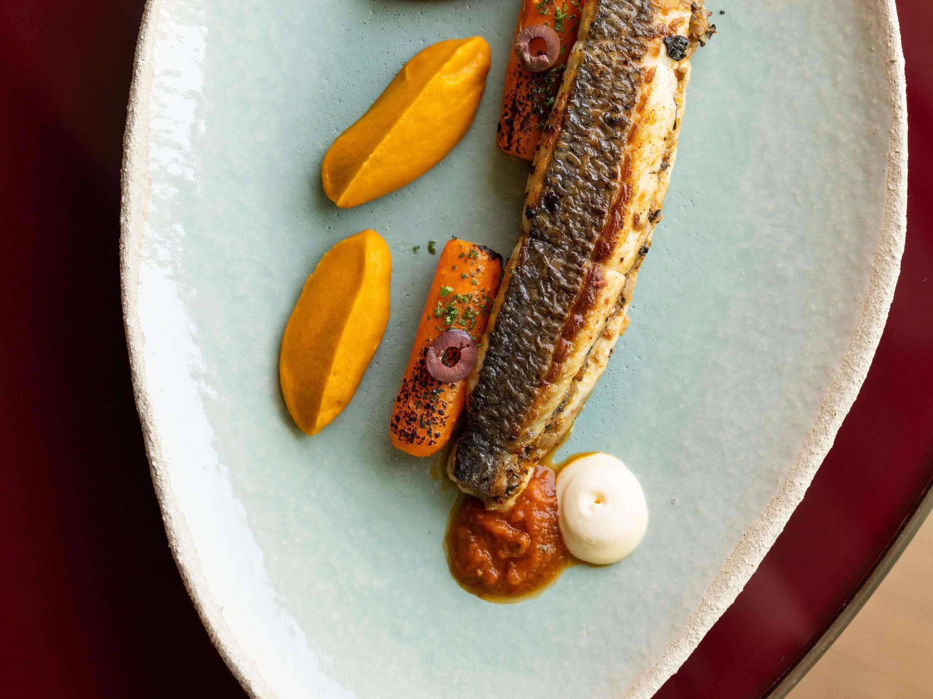 A plate with a fish fillet, two slices of mango, a carrot, and a dollop of sauce.