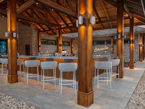 An outdoor bar area with wooden beams, stone walls, and white bar stools. - Sofitel Cotonou Marina Hotel & Spa (Cotonou)
