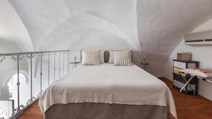 Ein Schlafzimmer mit einem großen Bett, einem kleinen Nachttisch, einem Spiegel und einem Fenster mit Blick auf einen Balkon.