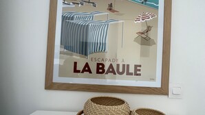 Póster enmarco de una escena de playa con el texto "ESCAPADE À LA BAULE" y dos cestas tejidas sobre una mesa blanca.