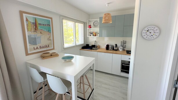 Una cocina moderna con armarios blancos, encimera de madera y un comedor con mesa y sillas blancas.