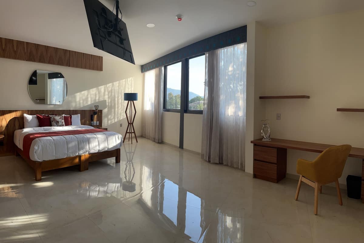 Habitación de hotel moderna con una cama grande, un escritorio, una silla y vistas al exterior a través de amplios ventanales.