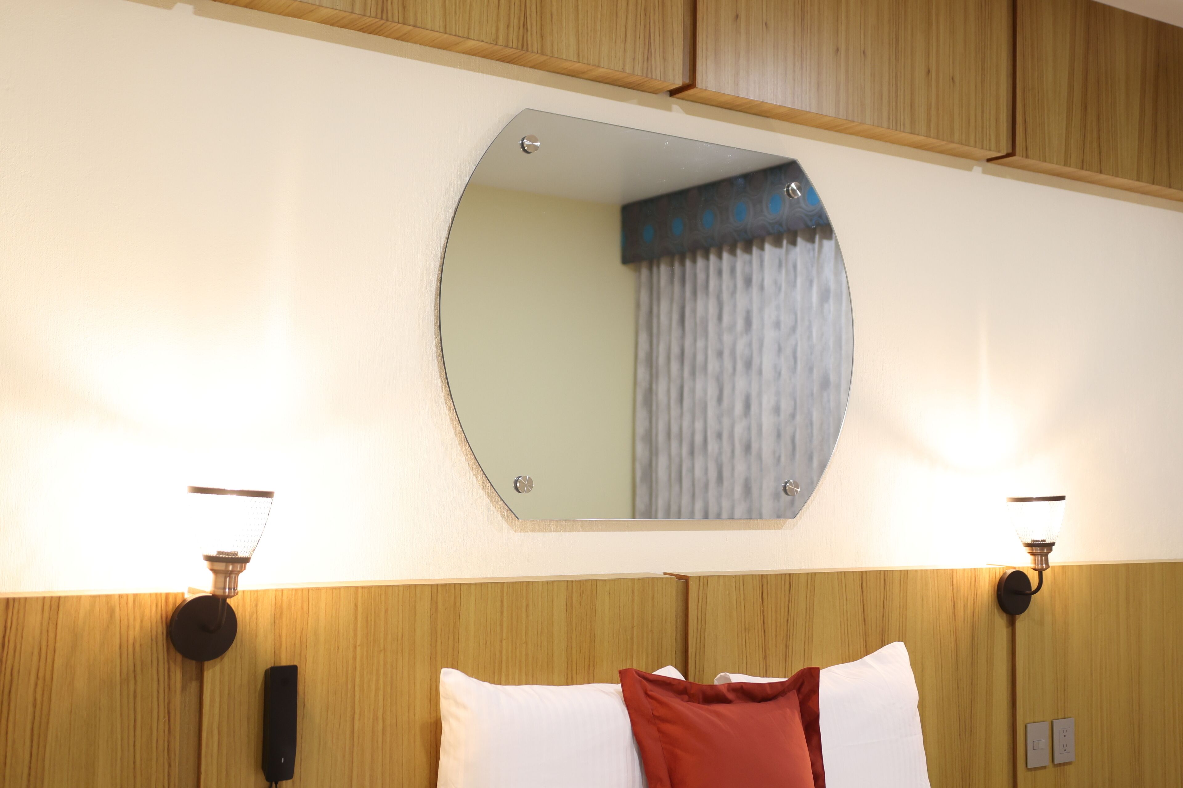 Een hotelkamer met een houten hoofdeinde, een ronde spiegel en twee wandlampen.
