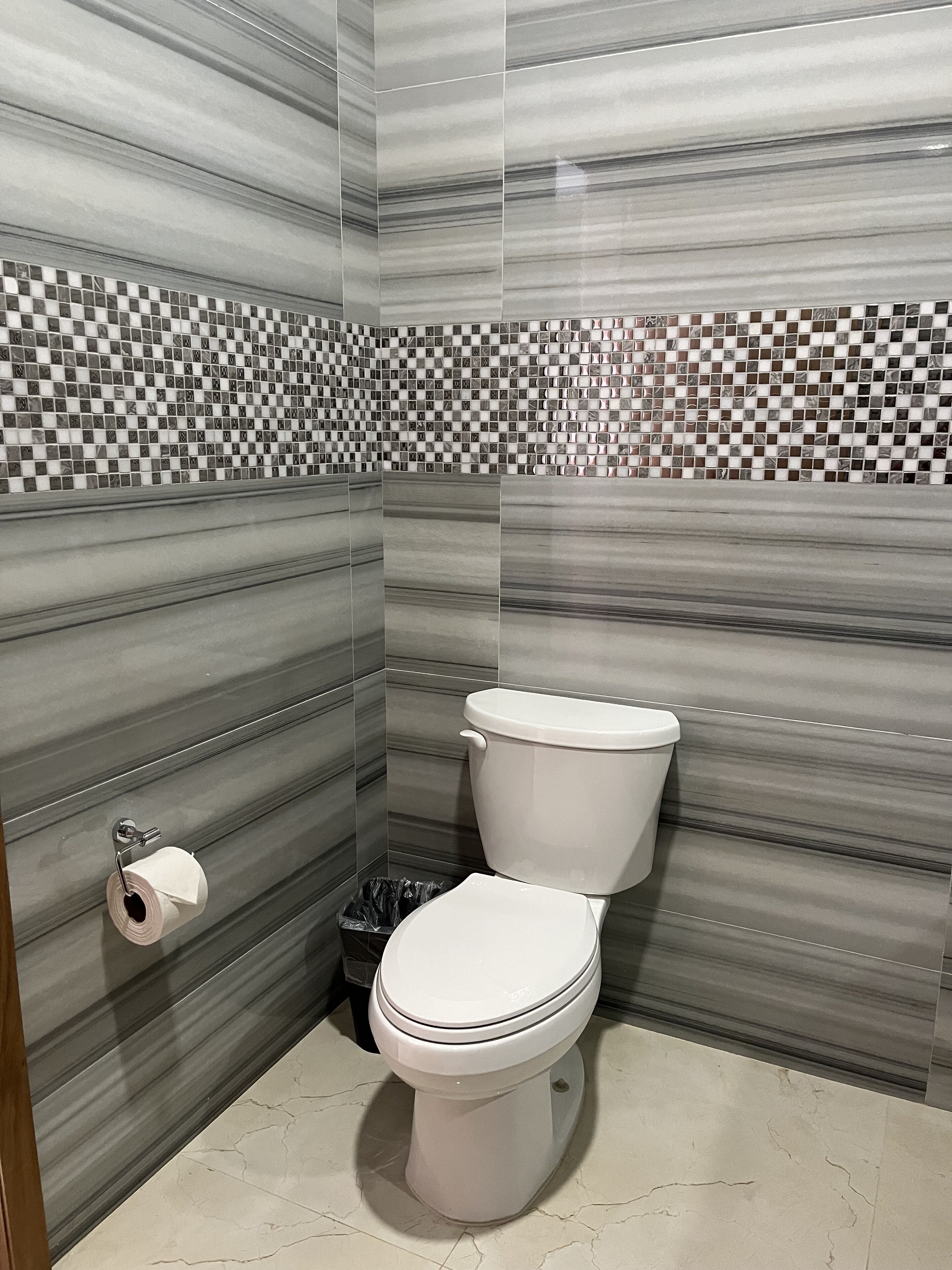 A bathroom with a toilet, a toilet paper holder, and a trash bin.