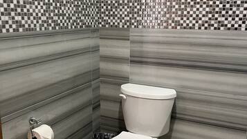 A bathroom with a toilet, a toilet paper holder, and a trash bin.