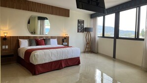 Una habitación de hotel moderna con una cama grande, un televisor de pantalla plana montado en la pared, un amplio ventanal con vistas y una lámpara de pie.