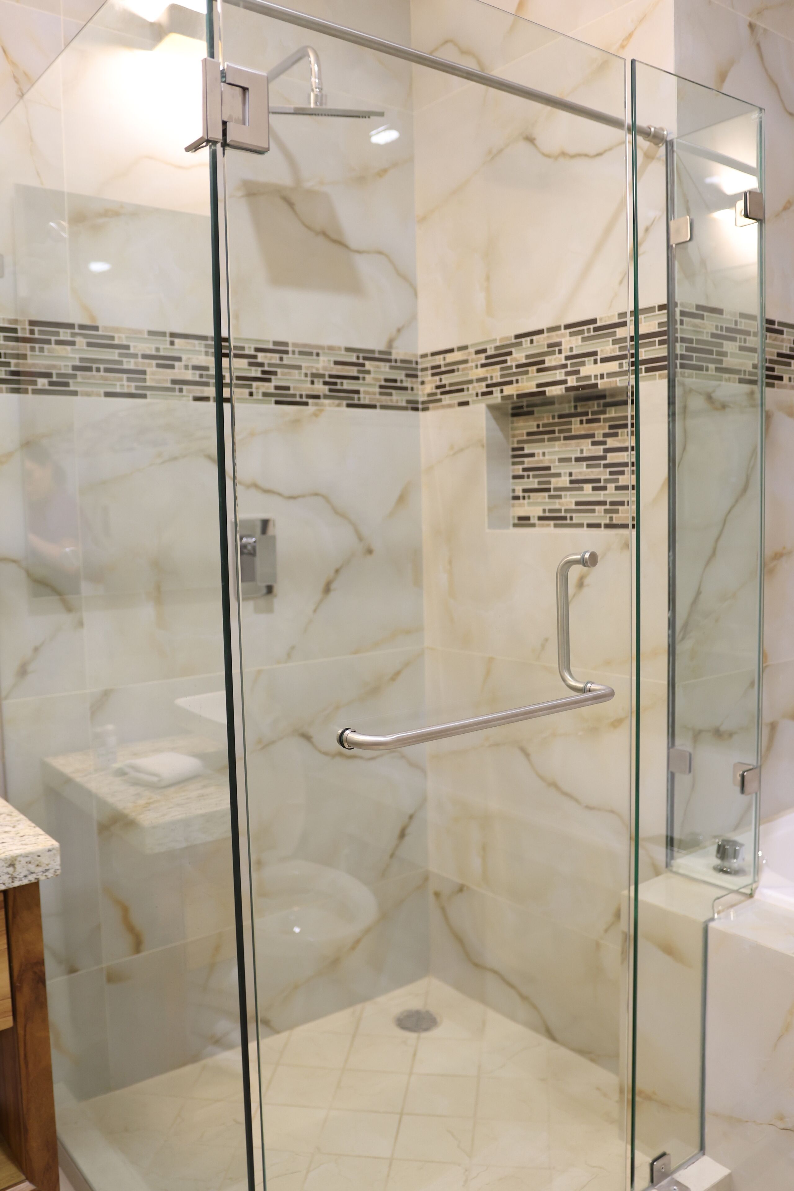 A glass-enclosed shower with a marble wall, a glass door, and a handrail.
