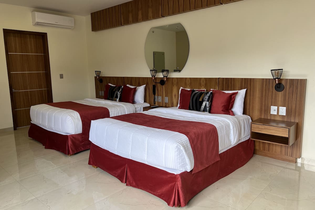 Habitación de hotel con dos camas, cabecera de madera, un espejo grande y una mesita de noche.