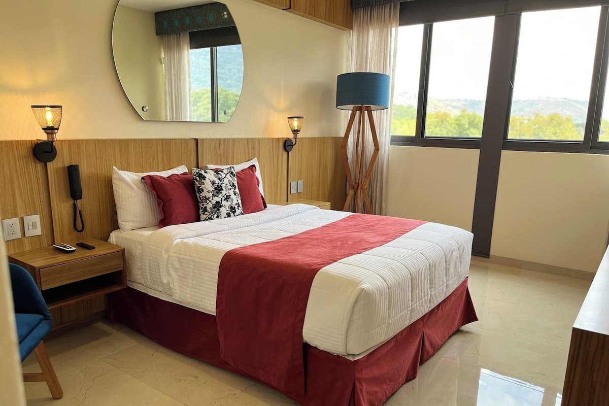 Habitación de hotel con una cama grande, lámparas de noche, un teléfono y vistas al exterior a través de una ventana.