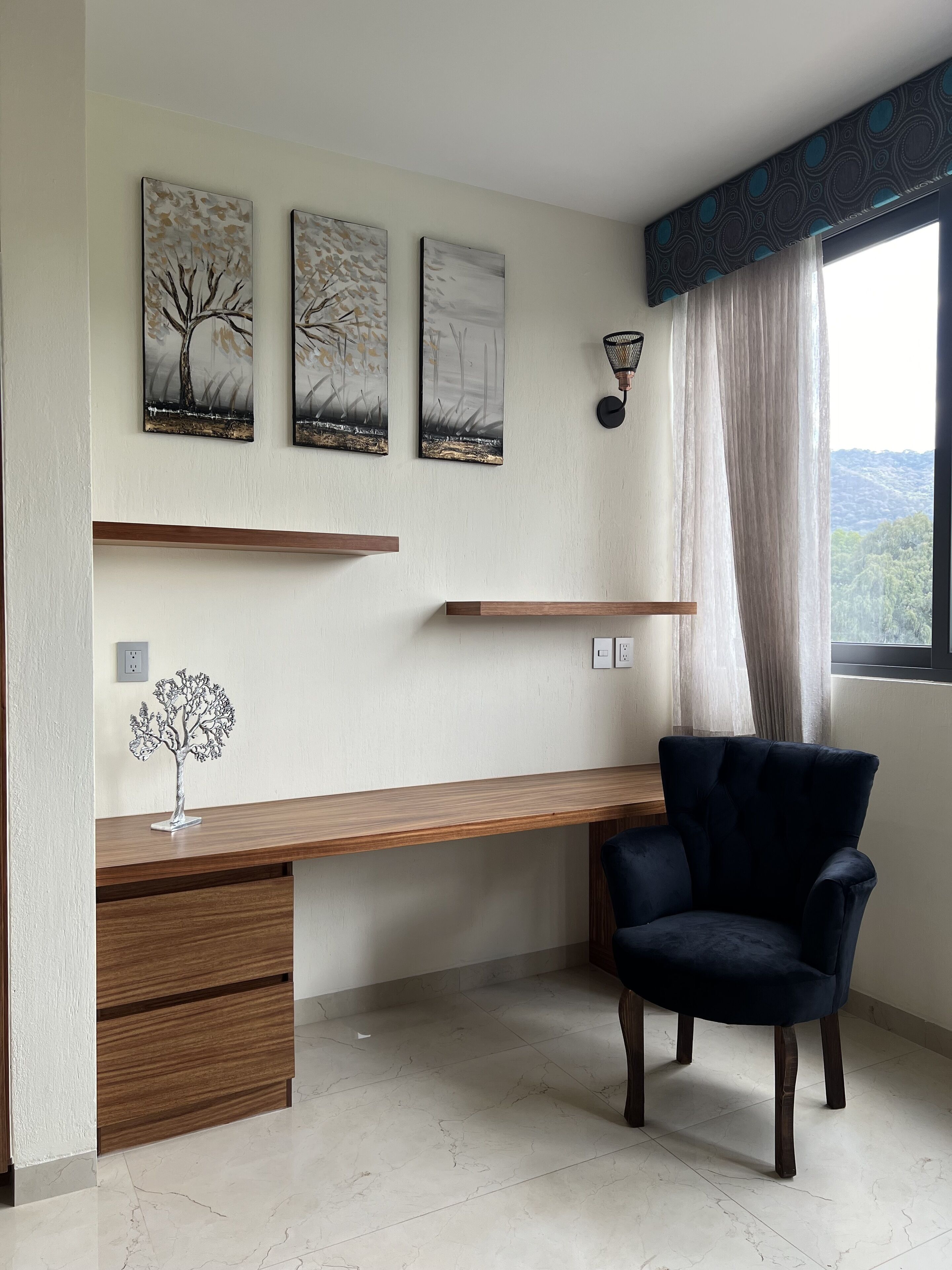 Um espaço de escritório moderno com uma mesa, cadeira e três quadros pendurados na parede.