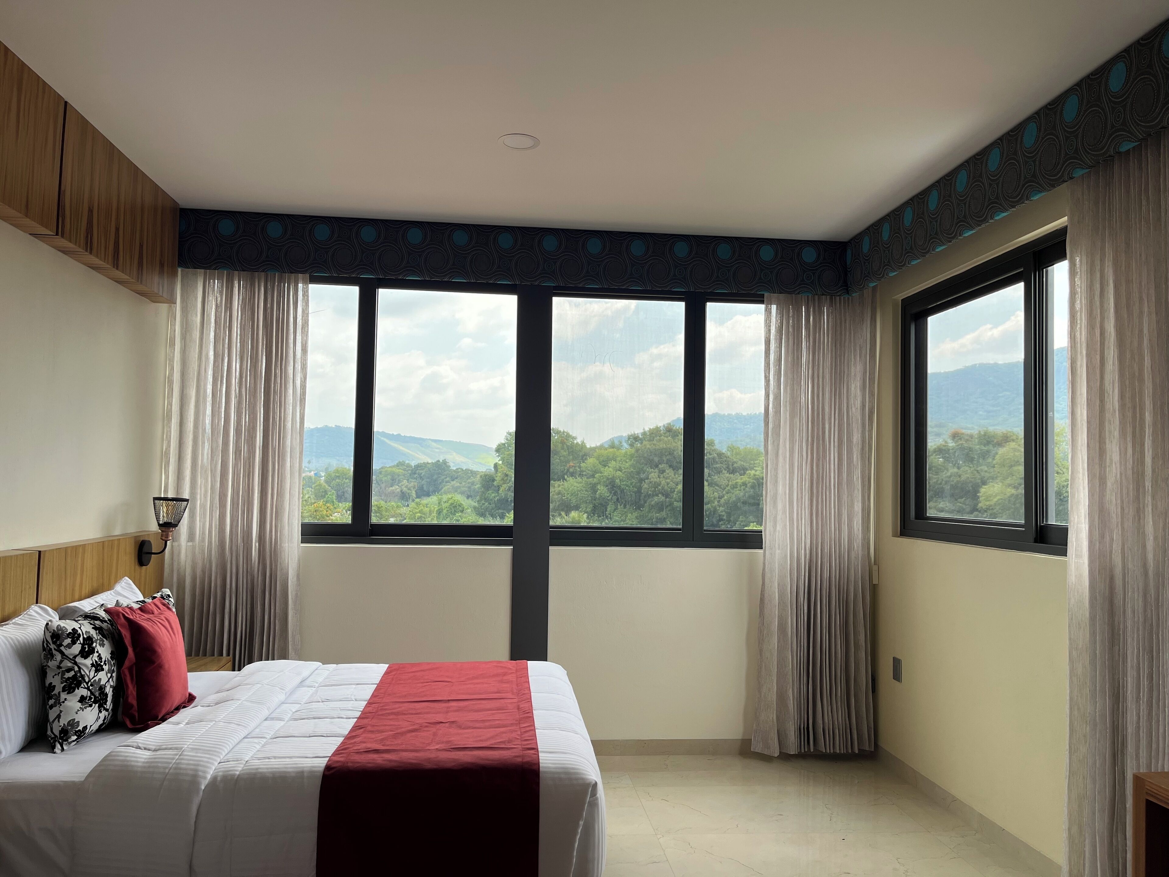 A hotel room with a large bed, a view of the outdoors through large windows, and a ceiling with a circular pattern.