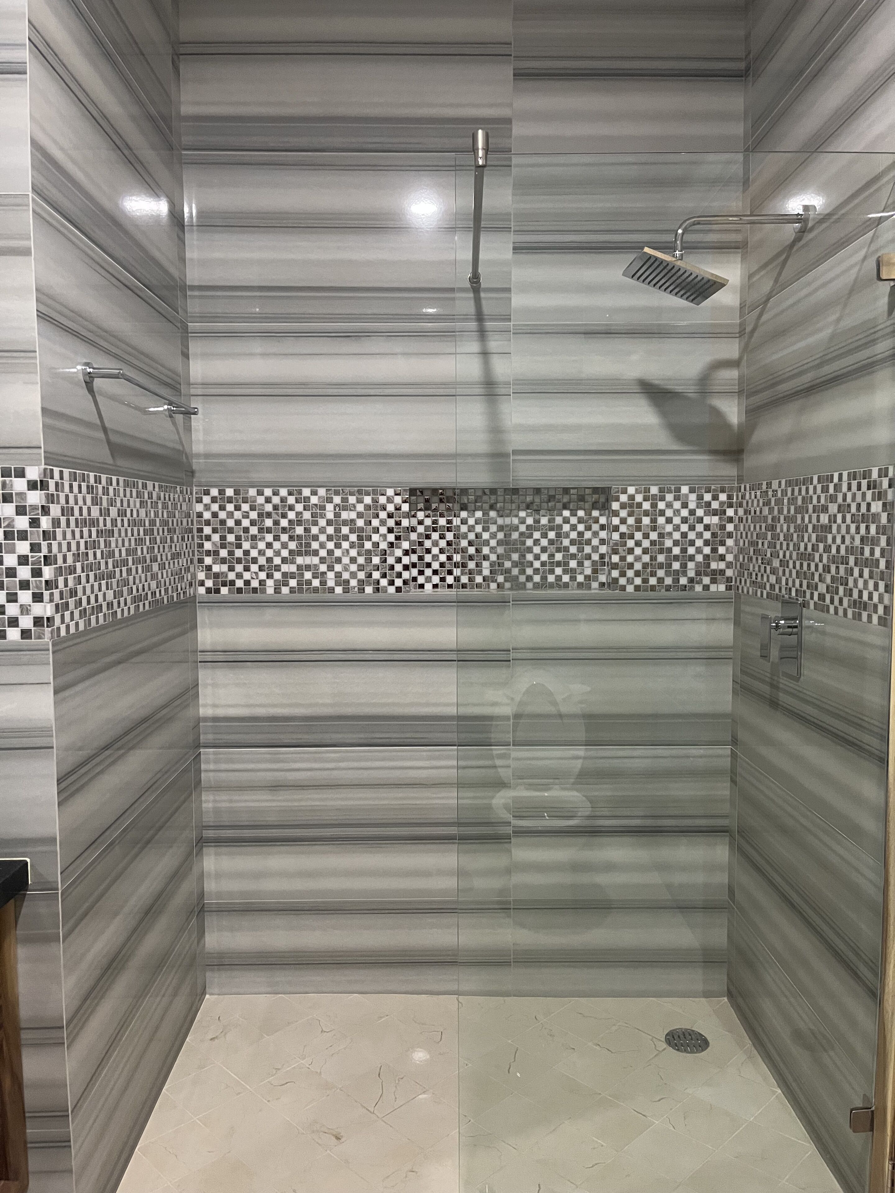 Um chuveiro moderno com porta de vidro, chuveiro de chuva e borda de azulejos xadrez.