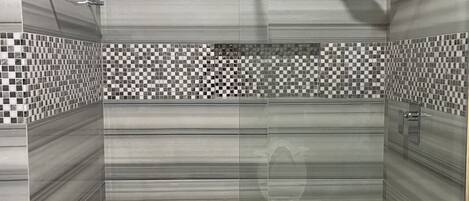 Una ducha moderna con puerta de cristal, cabezal de ducha de lluvia y un borde de azulejos a cuadros.