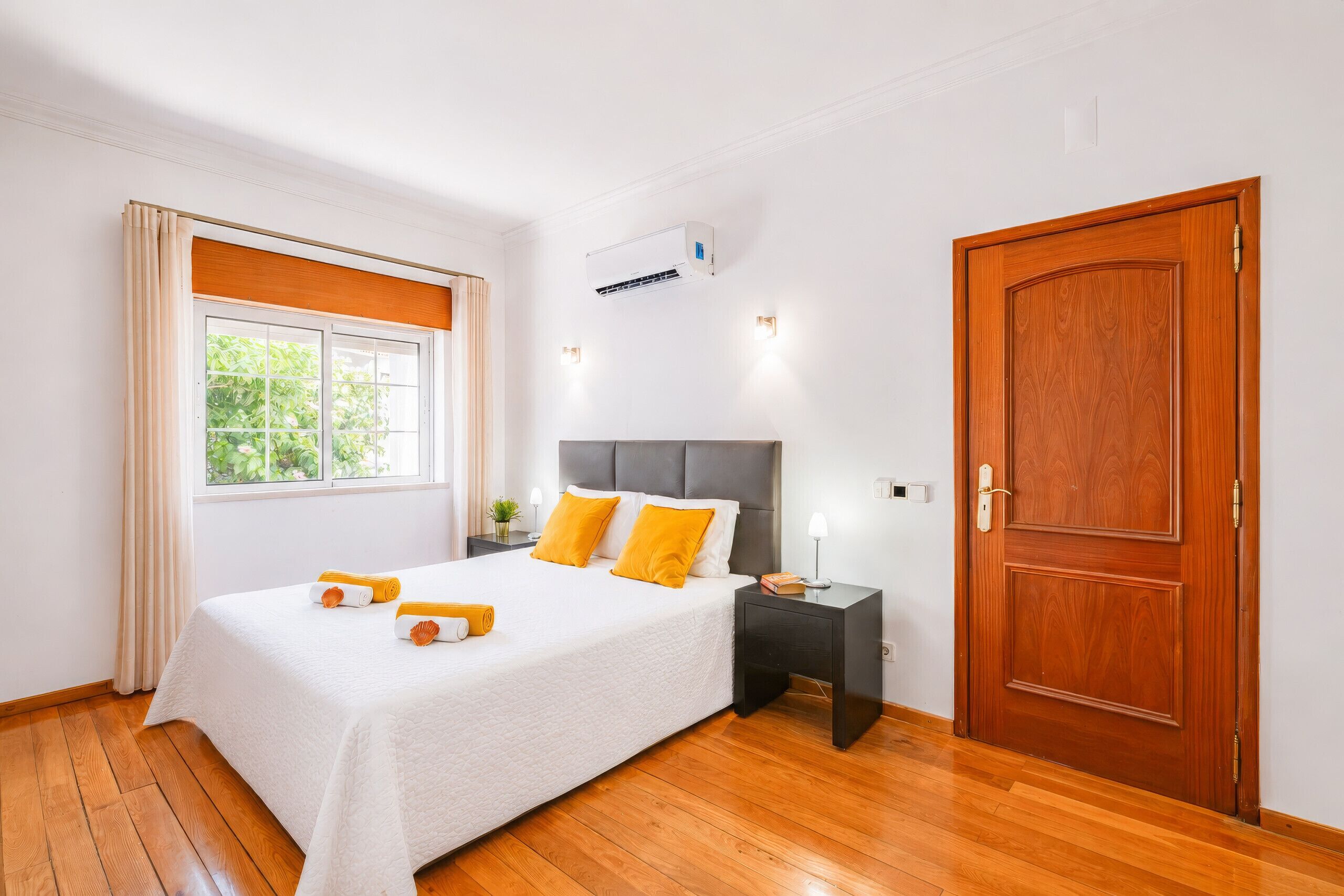 A hotel room with a bed, a nightstand, a wooden door, and a window with curtains.
